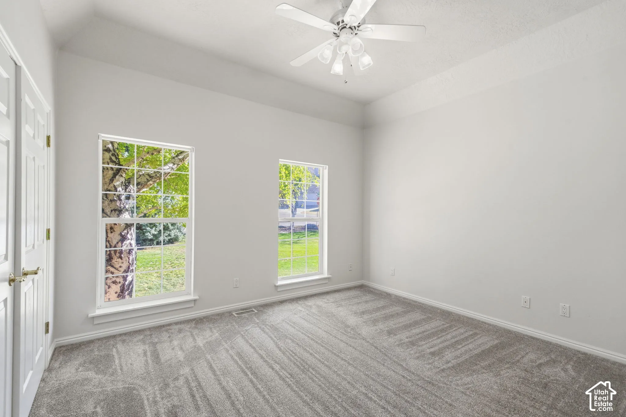 Interior room featuring a tray ceiling, plush carpeting, dual windows, and a ceiling fan with integrated lighting