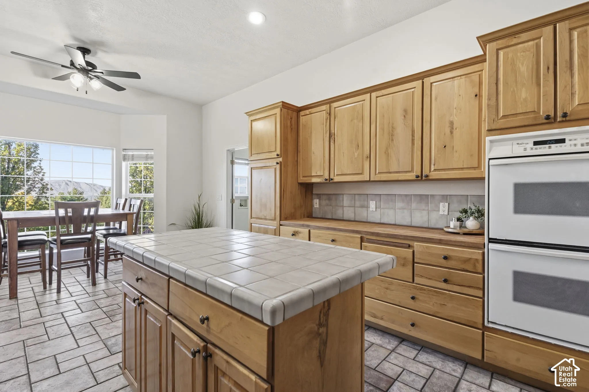 Kitchen featuring wood cabinetry, a central island with a tiled countertop, double wall ovens, tile flooring, and a multi-pane window assembly