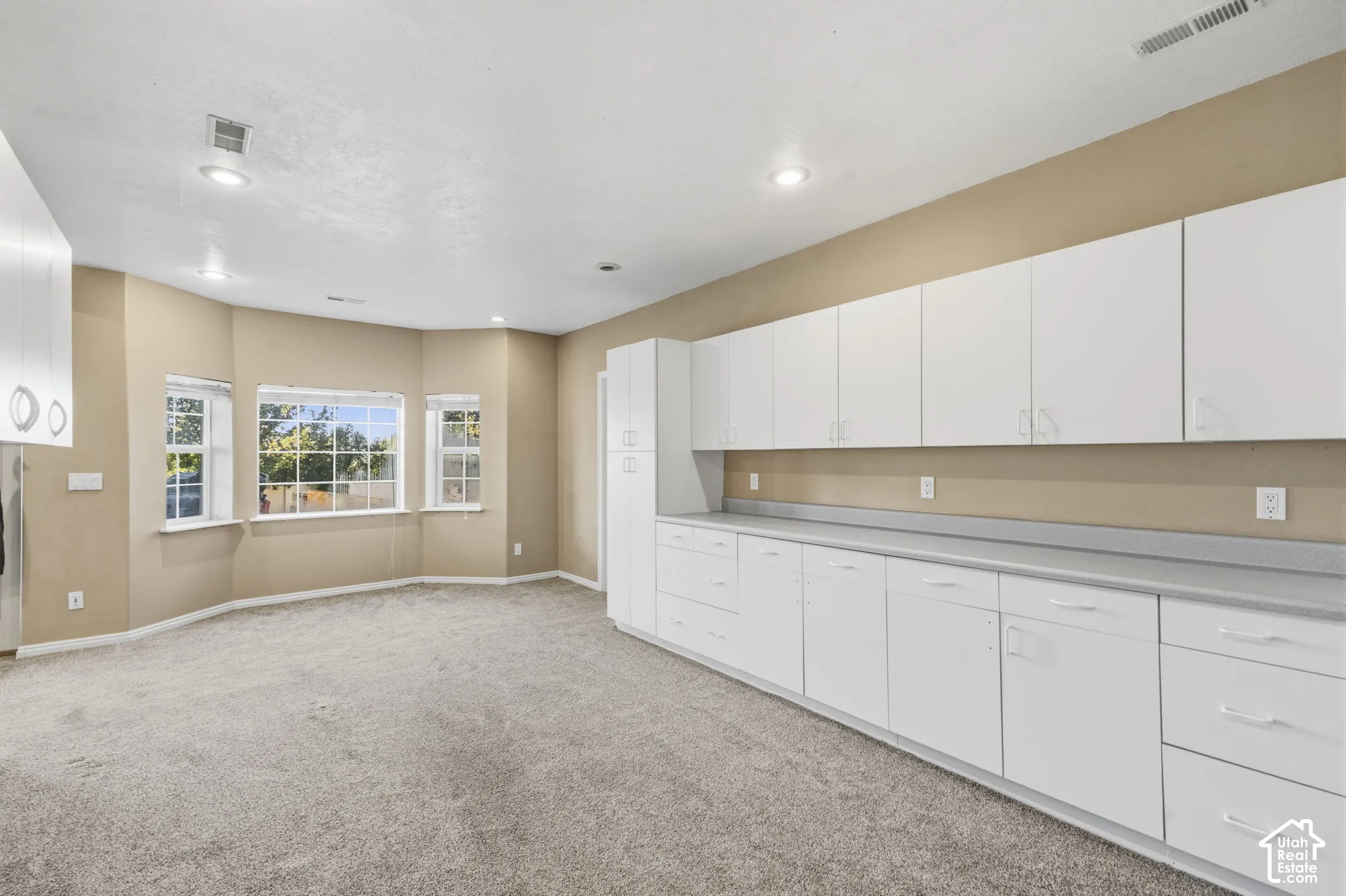 Expansive room featuring recessed lighting, a bay window, wall-to-wall carpeting, and floor-to-ceiling built-in white cabinetry with a solid-surface countertop