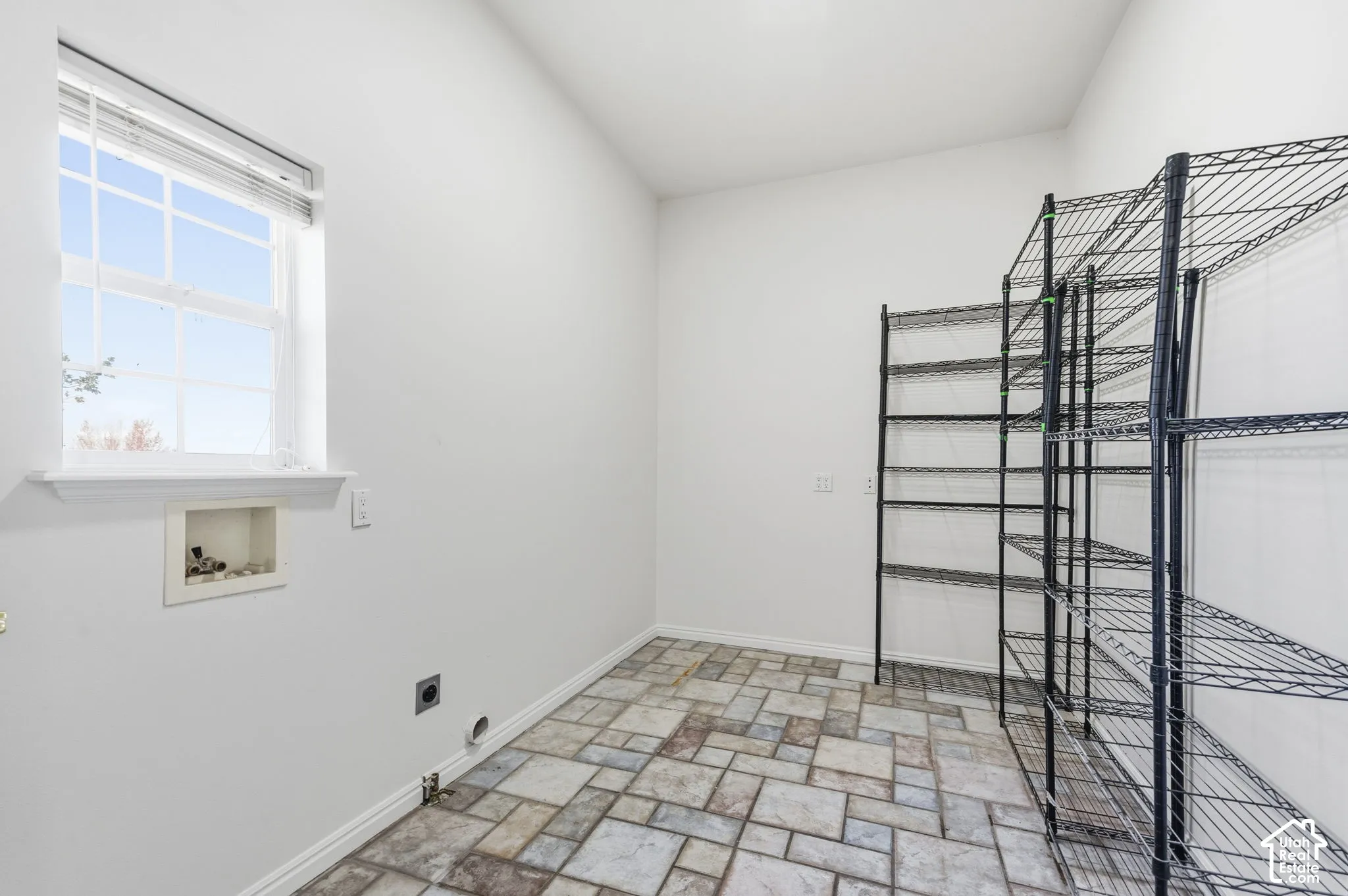 Utility room featuring multi-tonal stone-tile flooring, a recessed plumbing hookup, and a single-pane window with interior muntins