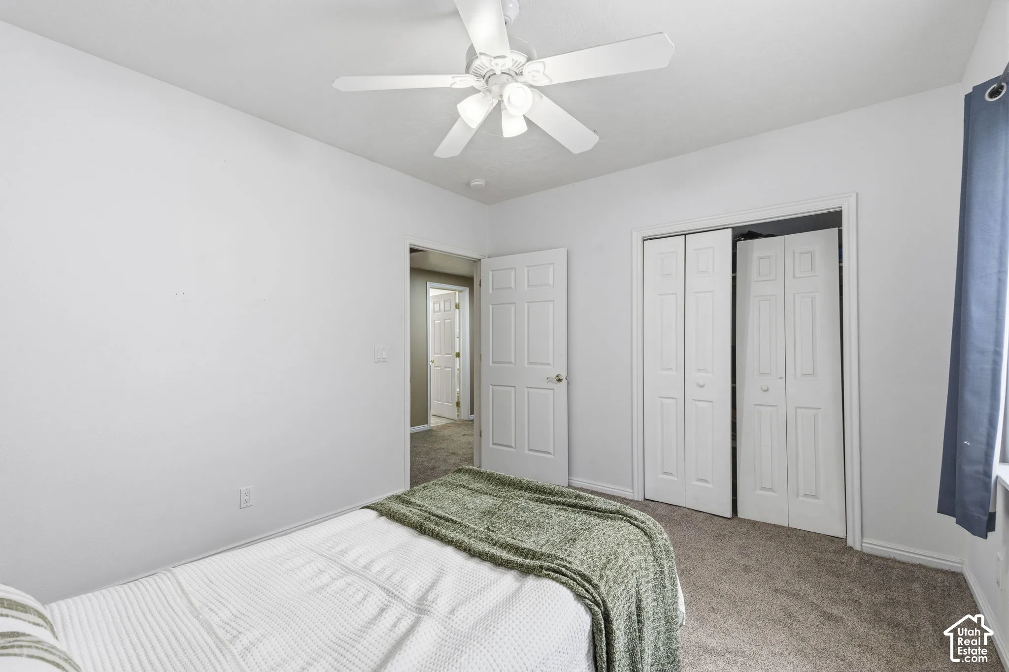 Neutral-toned wall paint, wall-to-wall carpeting, white six-panel interior doors, ceiling-mounted light fixture with a five-blade fan, and double-door reach-in closet with interior shelving