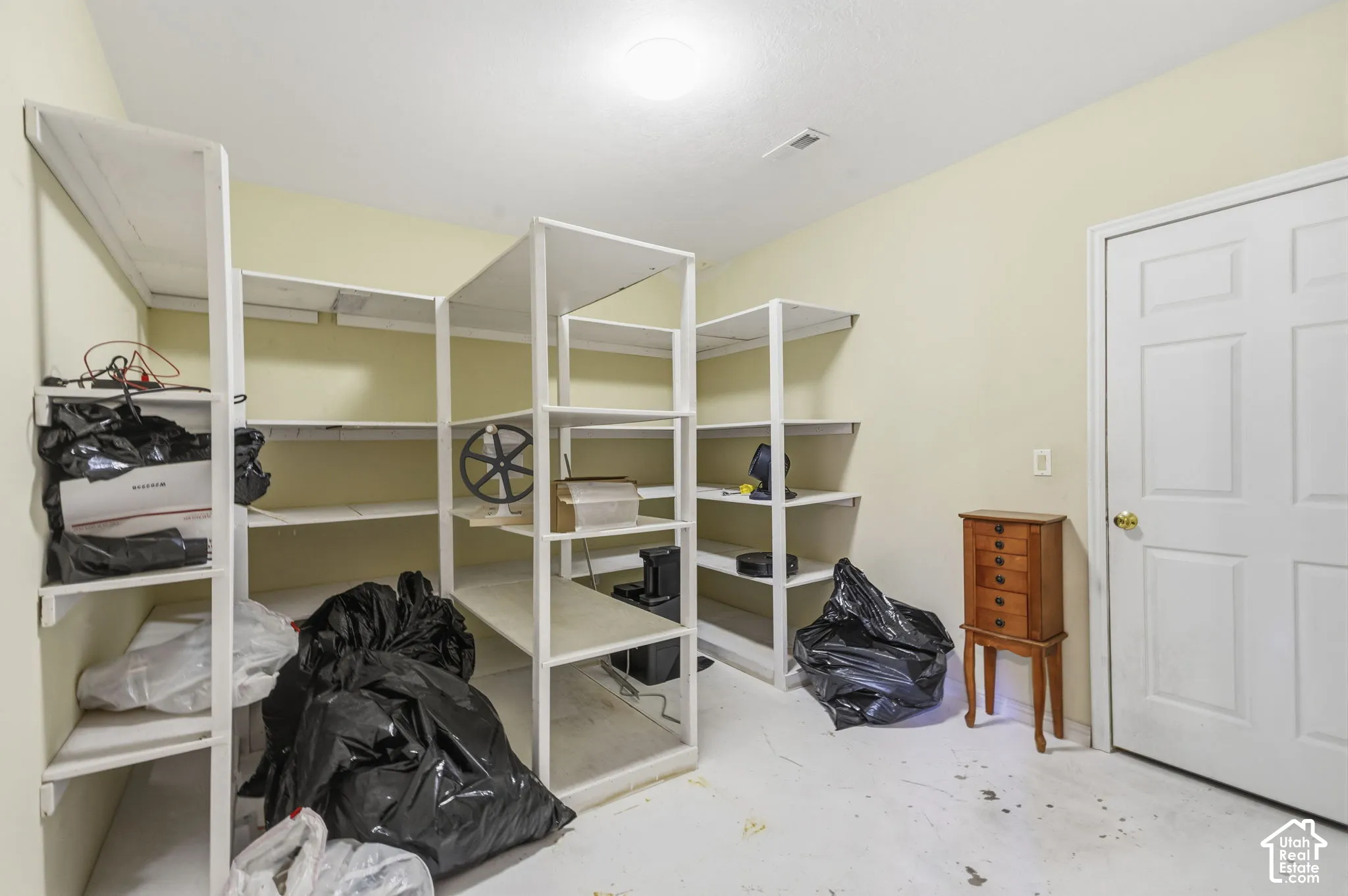 Storage room featuring white metal multi-level built-in shelving, painted concrete flooring, and a six-panel interior door