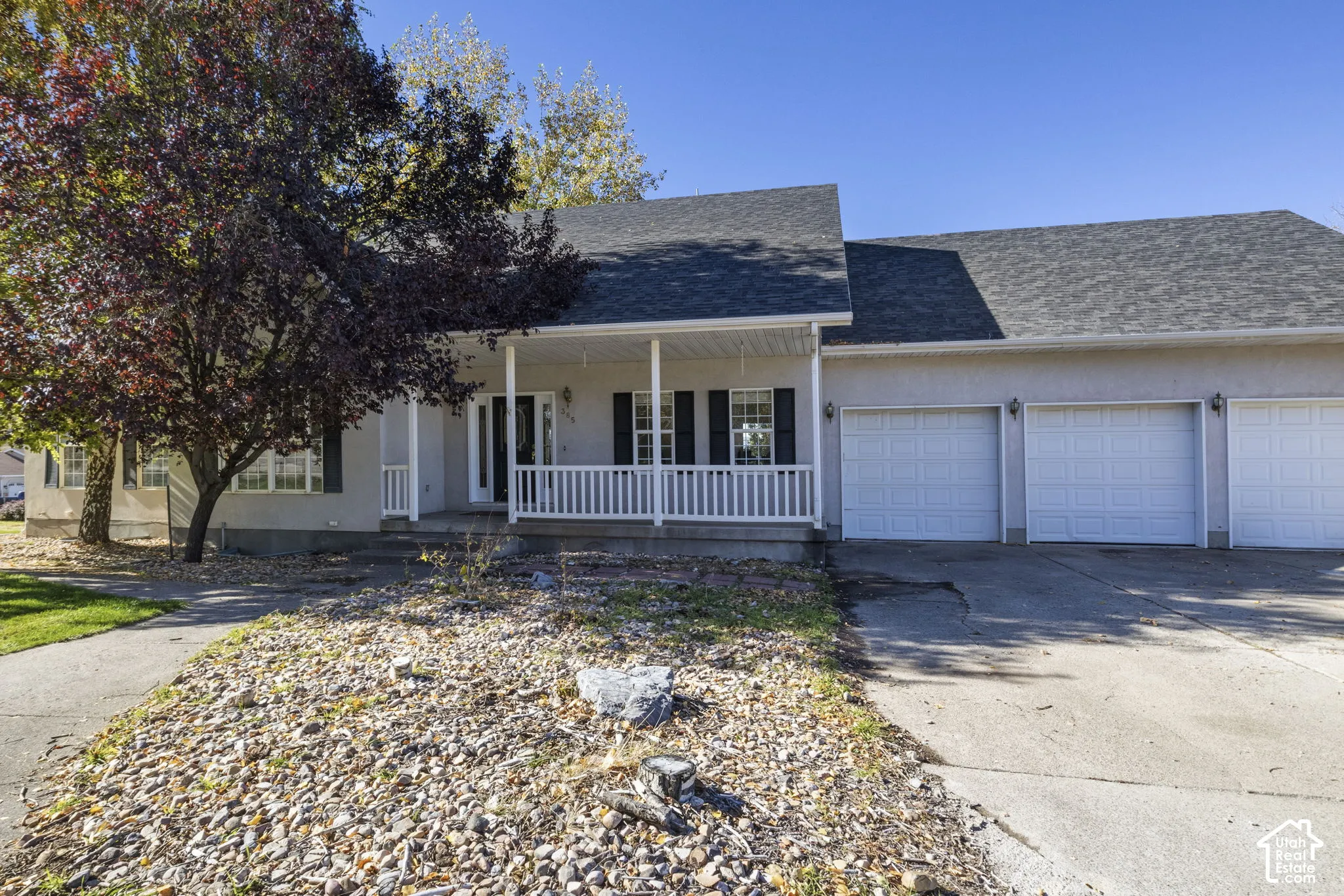Single-story exterior featuring a covered front porch with white railing, three-car garage, asphalt shingle roof, and decorative window shutters