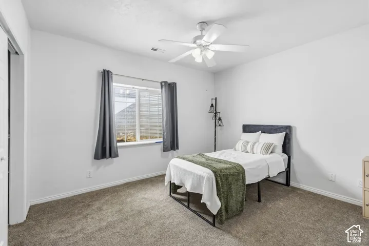 Neutral-toned carpeted flooring, white wall finish, slider window, and ceiling-mounted light fixture with integrated fan