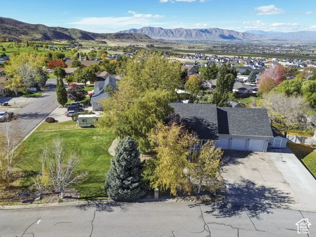 Aerial perspective featuring a multi-car garage, concrete driveway, mature landscaping, and mountain backdrop