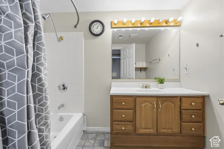 Bathroom featuring a wood-finish vanity with built-in storage drawers, a large wall-mounted mirror, a multi-bulb light fixture, and a white tiled tub surround