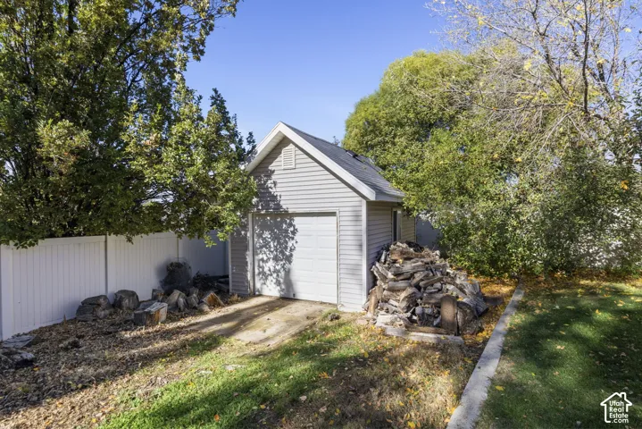 Detached garage with light-colored siding, a gabled roofline, and a solid-panel overhead door, situated within a fenced perimeter