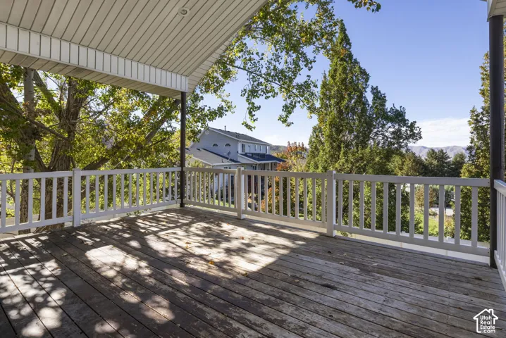 Covered deck featuring wood-plank flooring, white railing, and recessed ceiling lighting