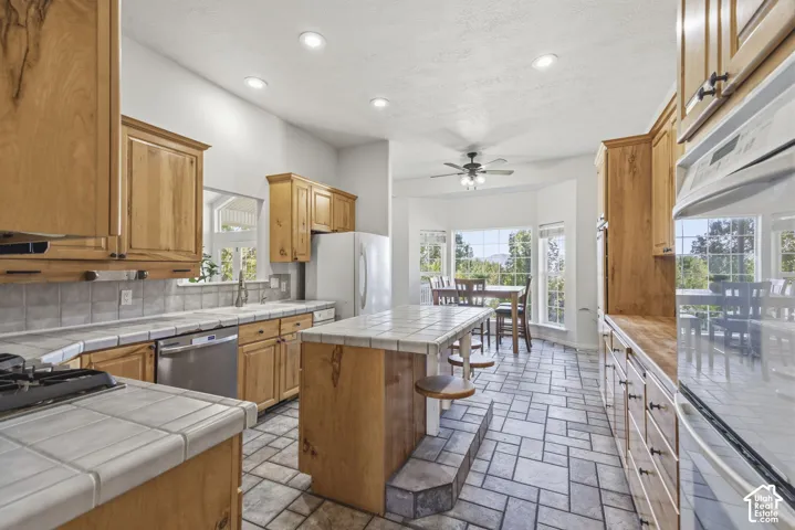Kitchen featuring wood cabinetry, tile countertops, a central island with bar seating, tiled flooring, and recessed lighting