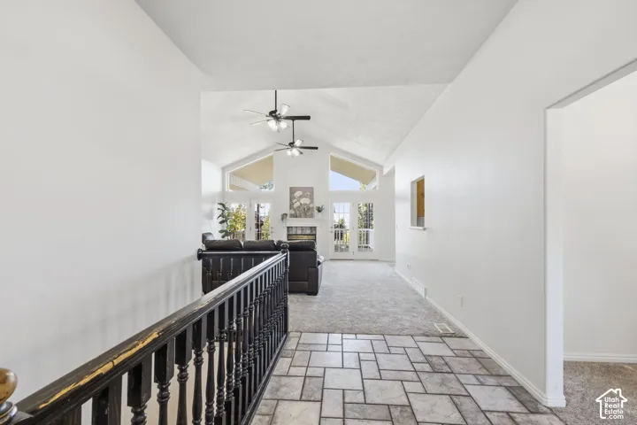 Vaulted ceiling with dual ceiling fans, tile flooring, stone-faced fireplace, and expansive windows