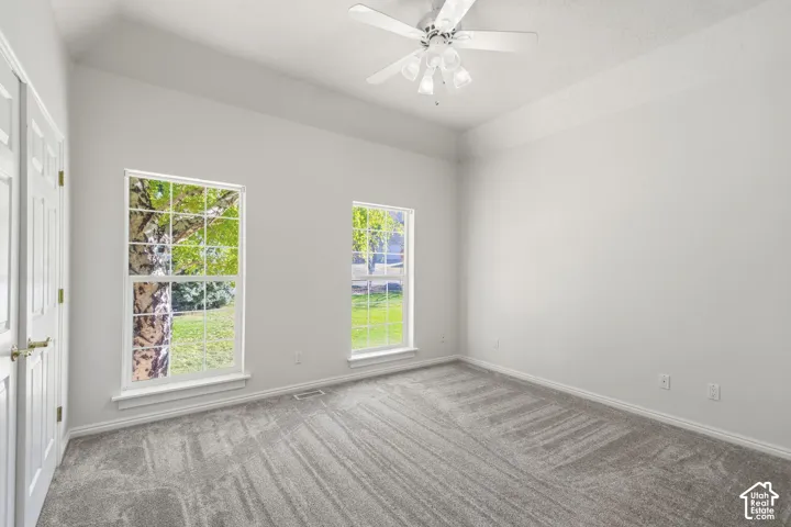 Interior room featuring a tray ceiling, plush carpeting, dual windows, and a ceiling fan with integrated lighting