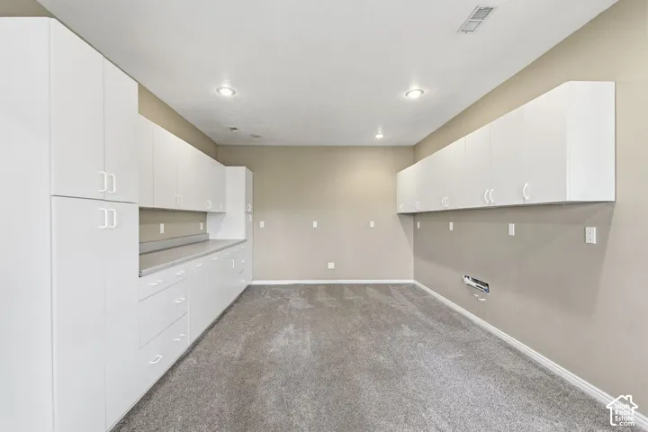Custom built-in white cabinetry, expansive countertop workspace, integrated recessed lighting, and wall-to-wall carpeting