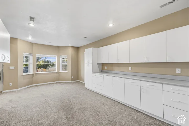 Expansive room featuring recessed lighting, a bay window, wall-to-wall carpeting, and floor-to-ceiling built-in white cabinetry with a solid-surface countertop