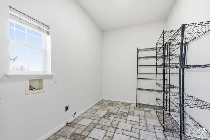 Utility room featuring multi-tonal stone-tile flooring, a recessed plumbing hookup, and a single-pane window with interior muntins