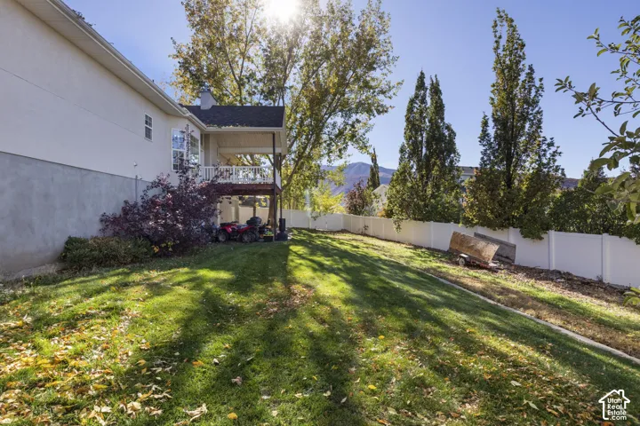 Backyard featuring a covered deck, white vinyl perimeter fencing, mature trees, and a mountain backdrop