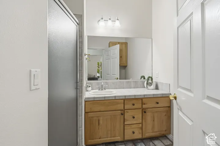 Bathroom featuring a wood-finish vanity with a tile countertop, integrated basin, oversized wall-mounted mirror, and three-bulb vanity lighting