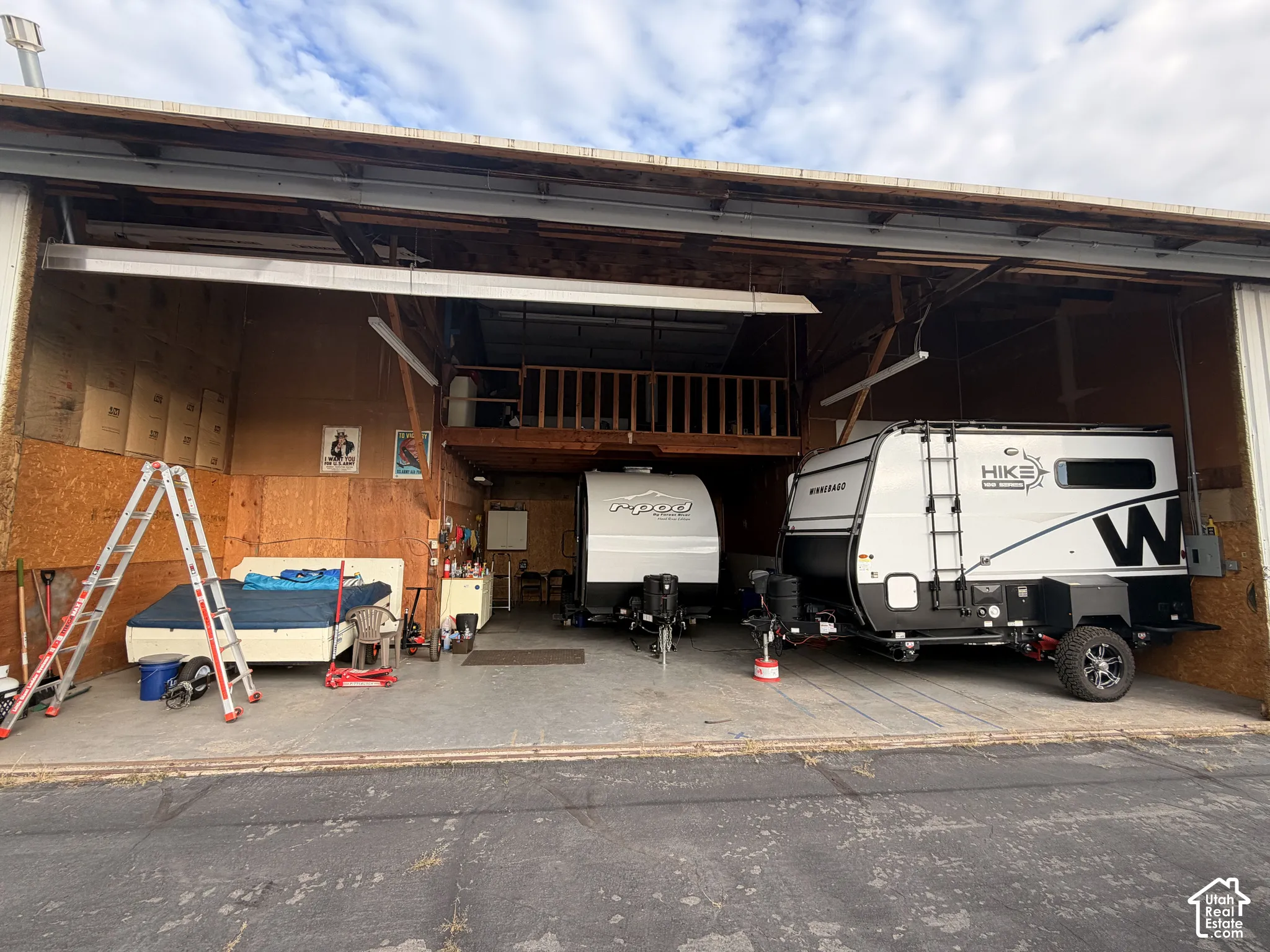 Expansive storage structure featuring a concrete floor, open-bay entry, elevated mezzanine loft, and exposed timber frame construction