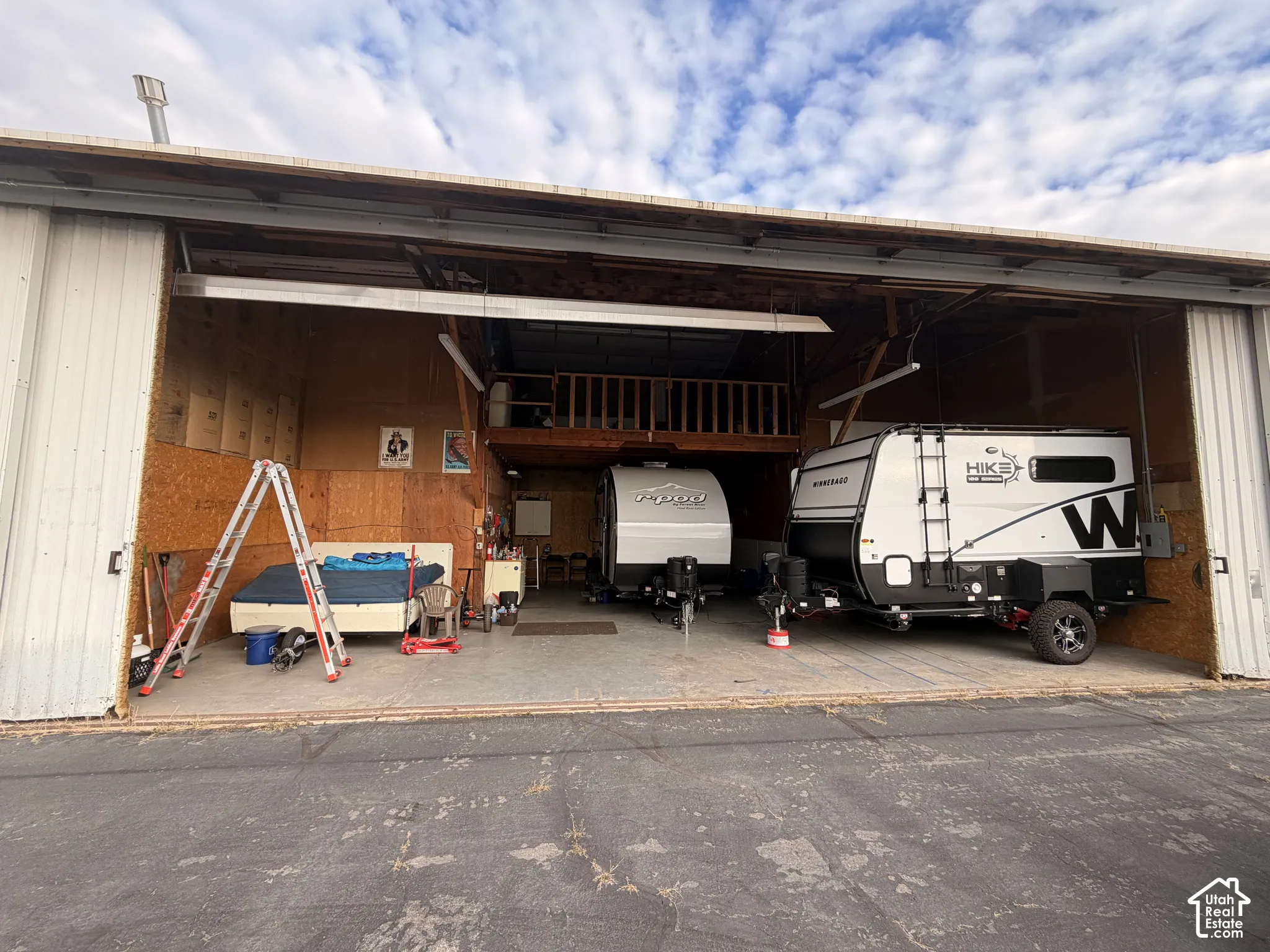 Metal-sided detached workshop featuring a high-clearance overhead door, expansive interior concrete flooring, and a built-in mezzanine loft