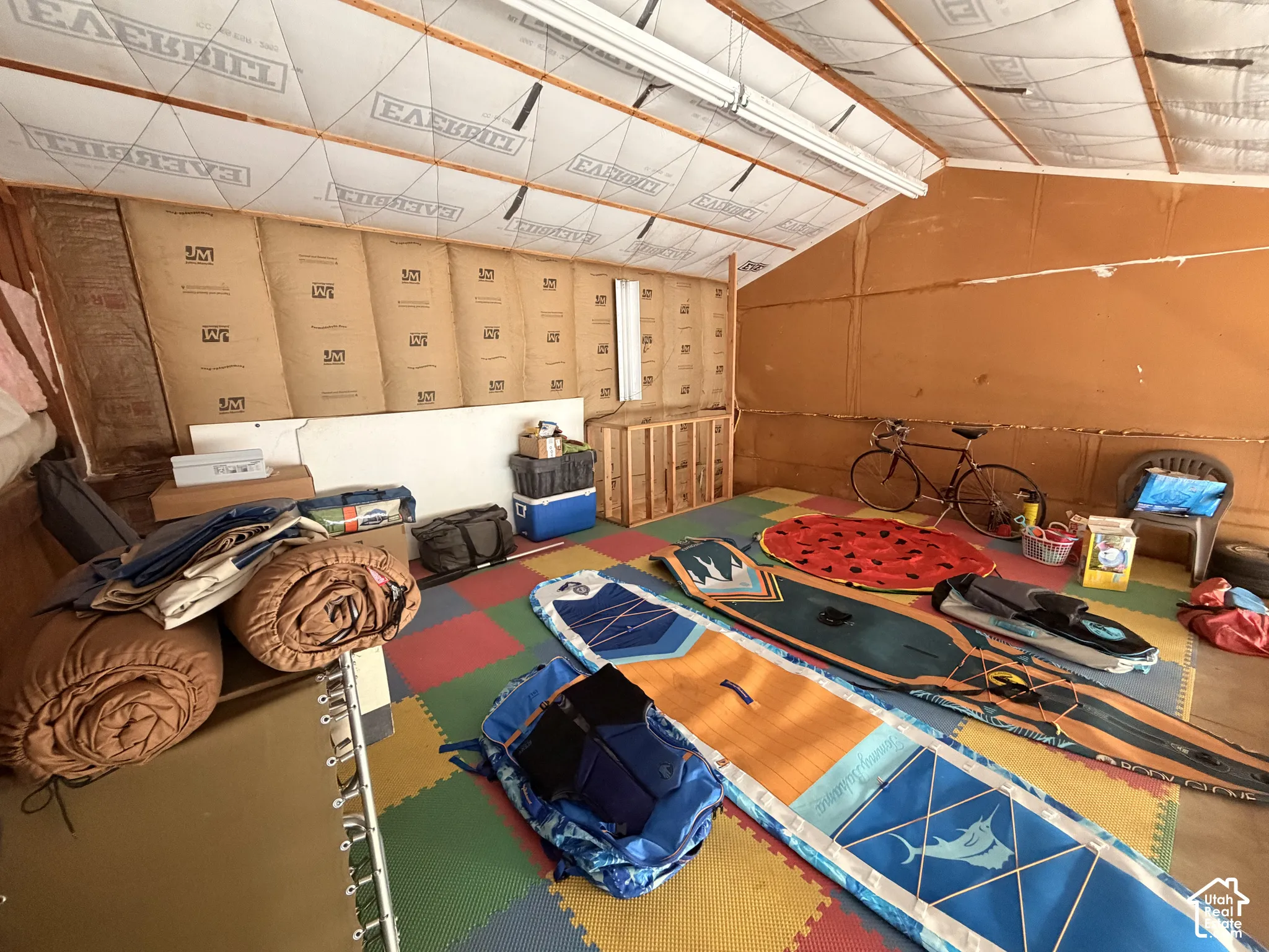 Interior space featuring insulated walls, an exposed beamed ceiling, and linear fluorescent lighting