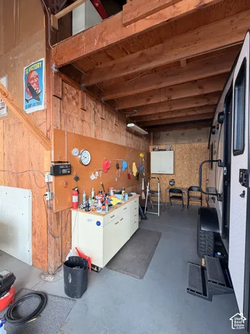 Enclosed workshop space featuring exposed timber framing, built-in storage cabinetry, a wall-mounted pegboard system, and high-clearance overhead ceilings
