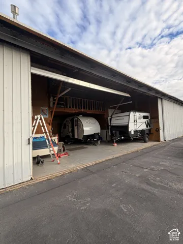 Large-scale workshop featuring high-clearance sliding metal doors, a concrete floor, and an integrated elevated storage loft
