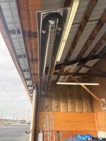 Ceiling-mounted infrared tube heater, exposed timber framing, and fluorescent shop lighting
