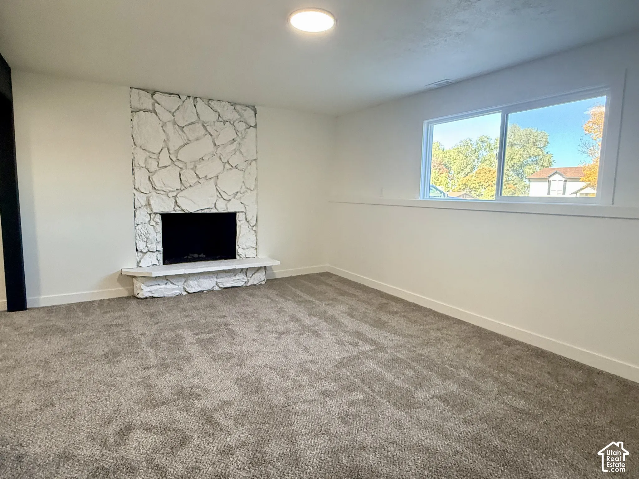 Fireplace featuring white stone masonry and a hearth, wall-to-wall carpeting, and a wide sliding window