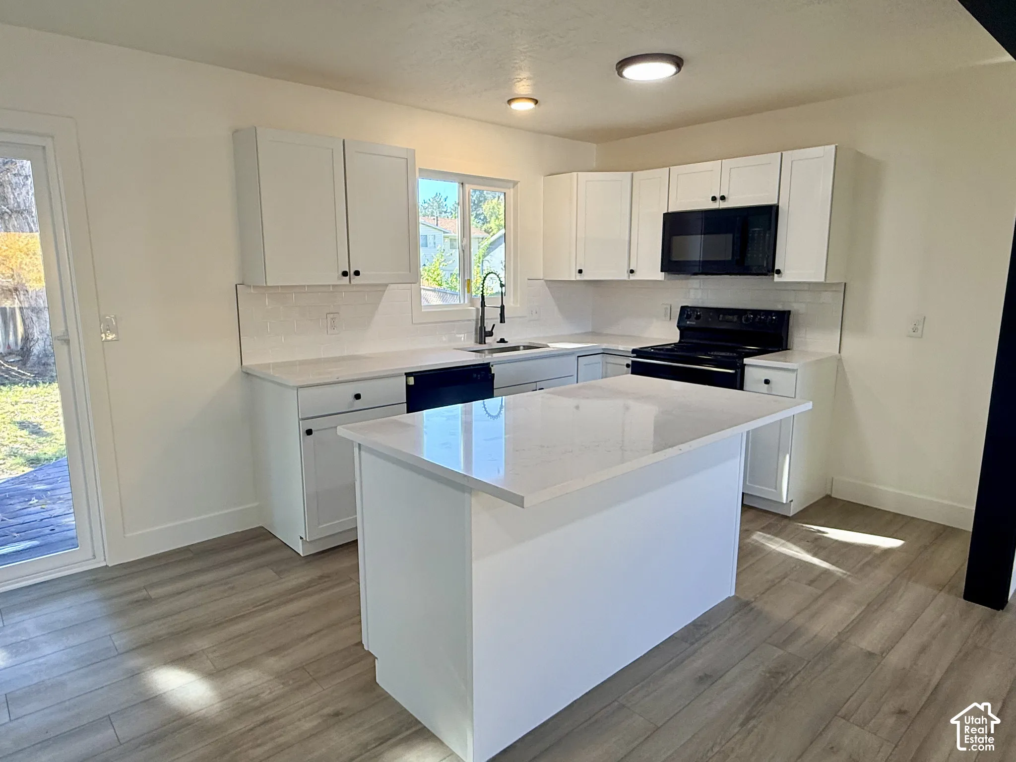 Kitchen featuring white cabinetry, an island with stone-finish countertop, subway tile backsplash, wood-finish flooring, and a sliding glass door