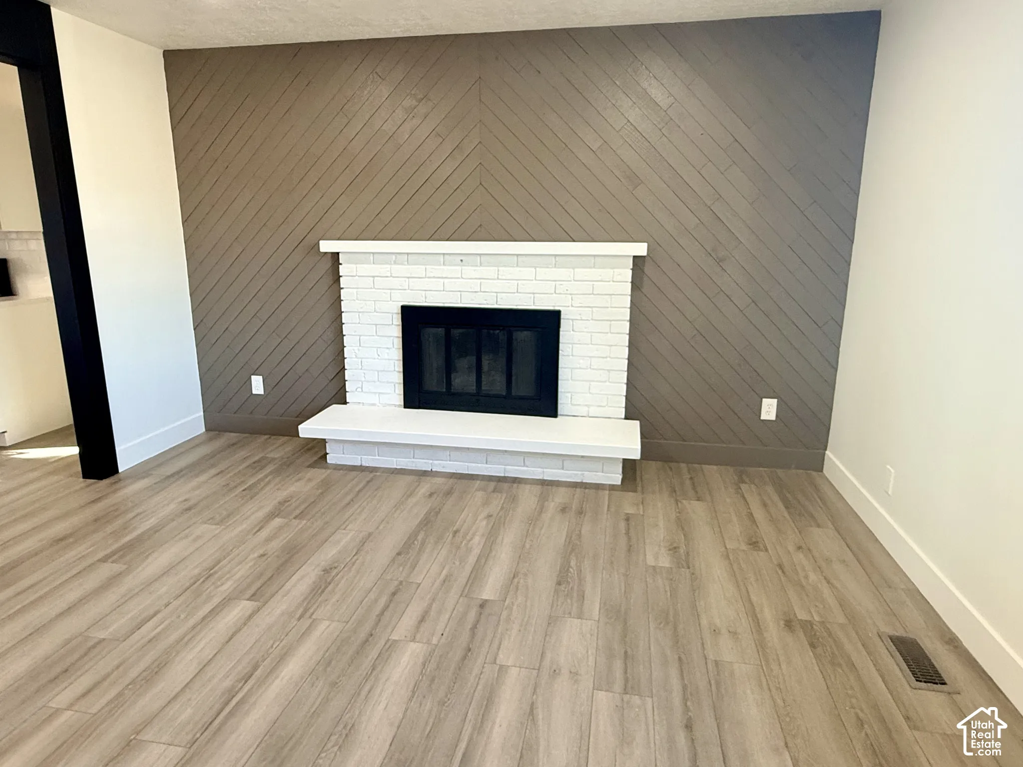 Chevron-patterned wood-finish accent wall, white brick fireplace with a concrete hearth, and wood-finish flooring