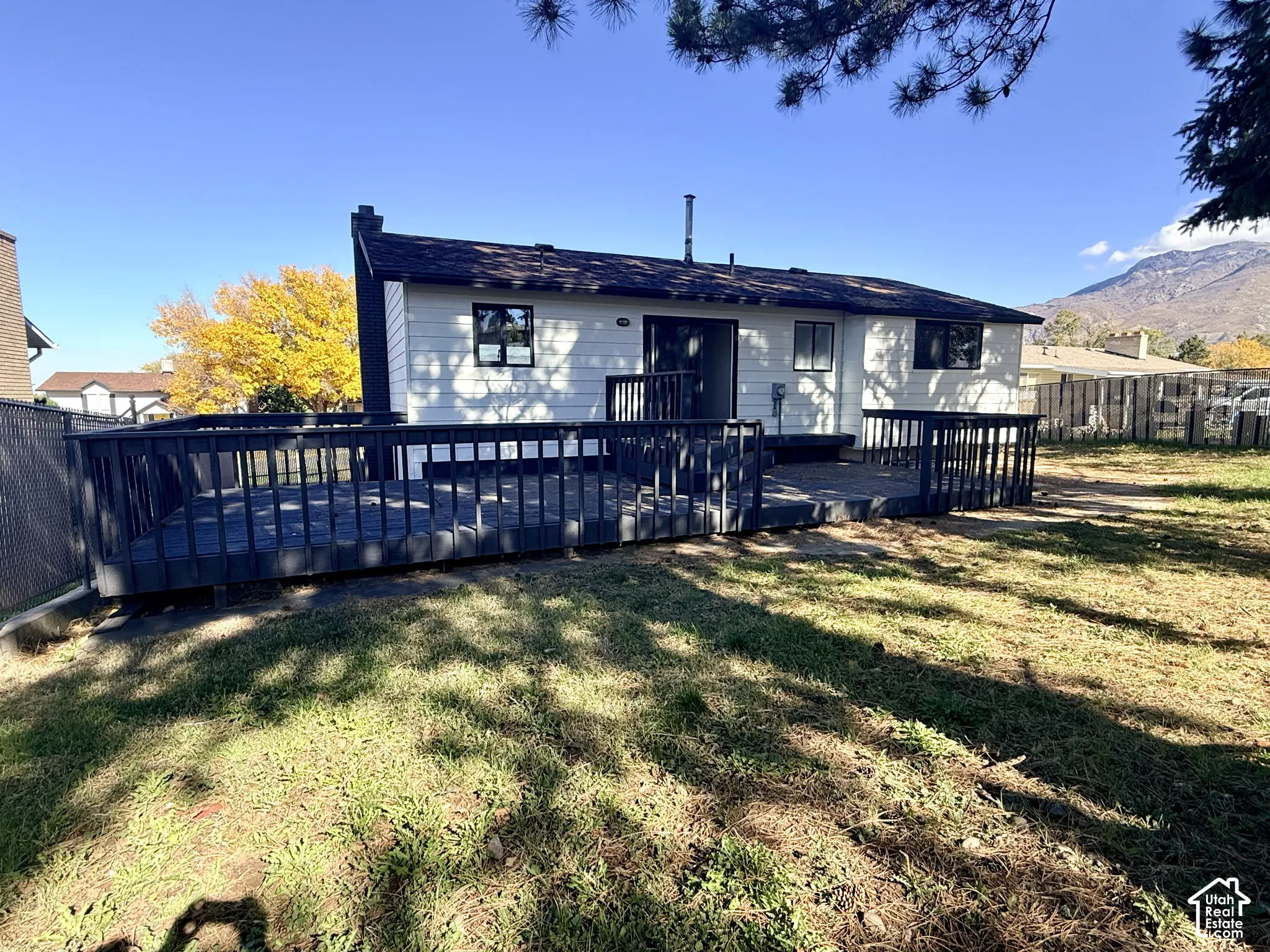 Exterior featuring white siding, a large raised wood deck with dark railings, and a mountainous backdrop
