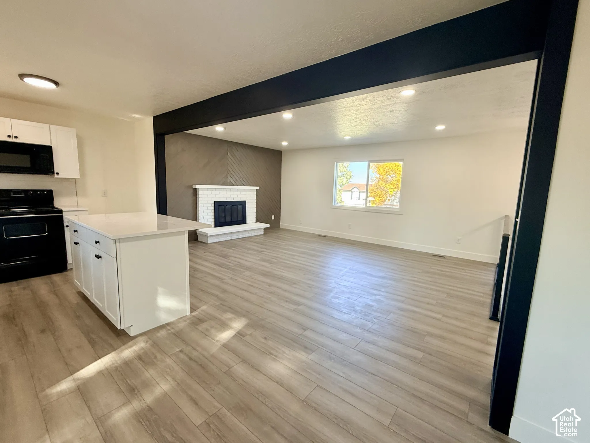 Kitchen featuring a central island with a solid-surface countertop, wood-finish flooring, recessed lighting, and a brick-surround fireplace with a hearth