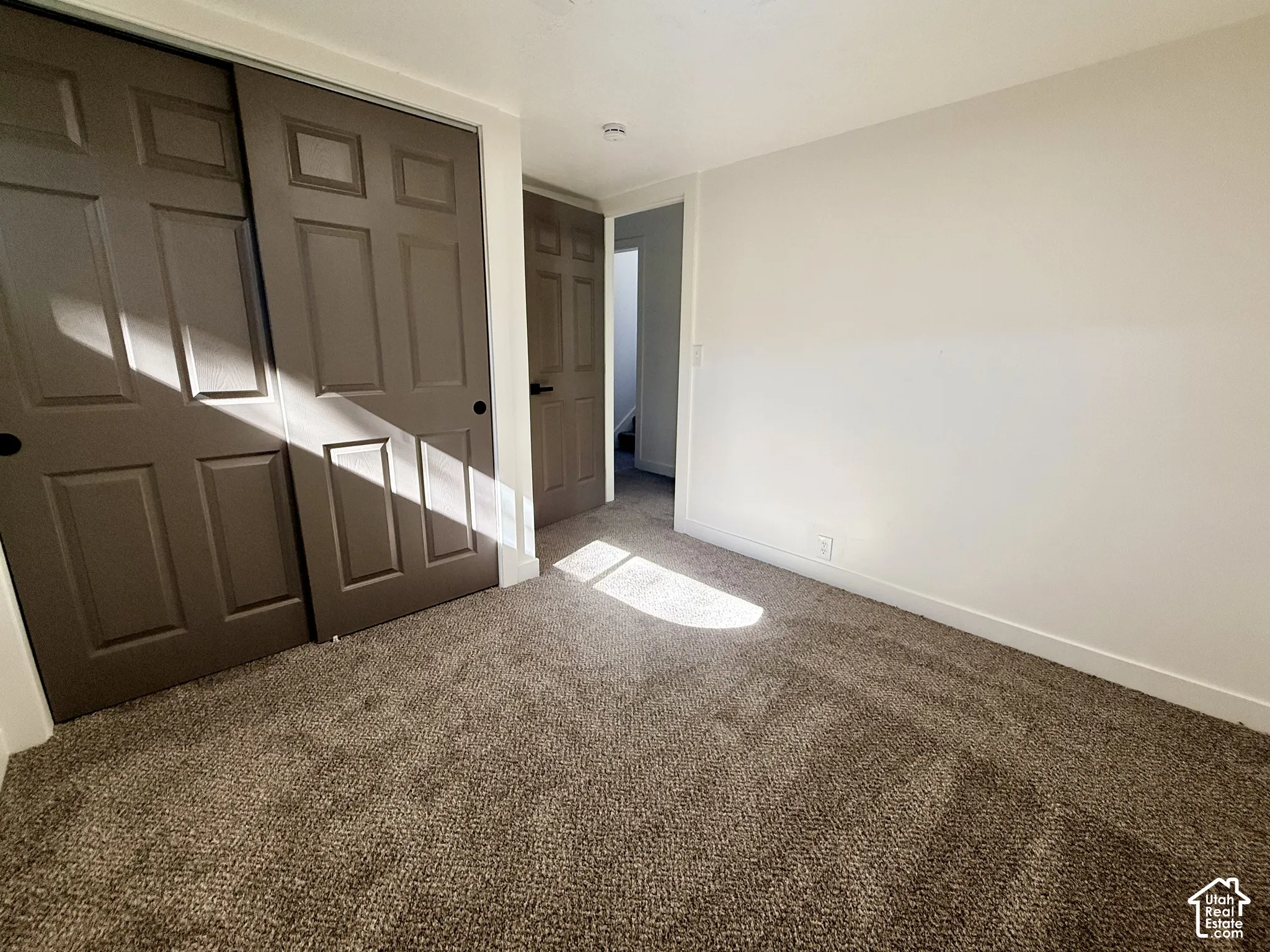 Neutral interior space featuring neutral wall paint, textured wall-to-wall carpeting, and sliding panel doors with recessed panels