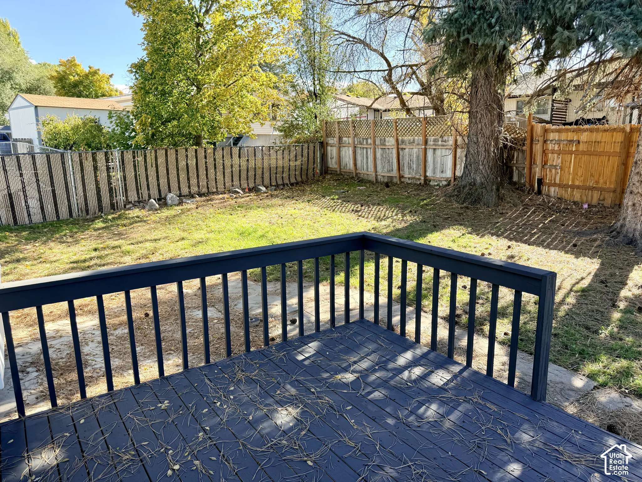 Elevated dark-stained wood deck featuring a protective perimeter railing, overlooking a fenced backyard with mature trees