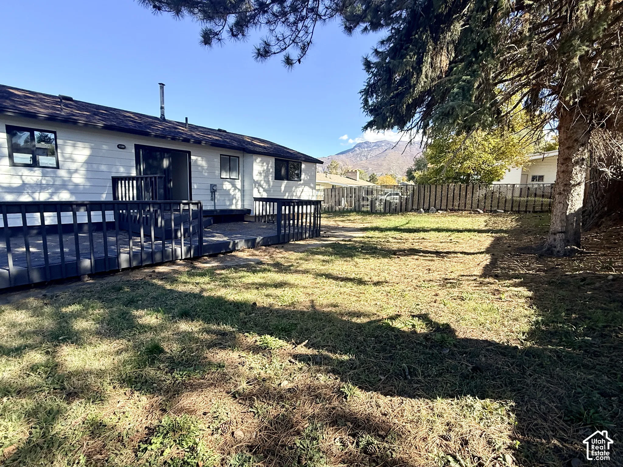 Exterior features include horizontal siding, a raised wood deck with balustrades, a fenced perimeter, and a mountain backdrop