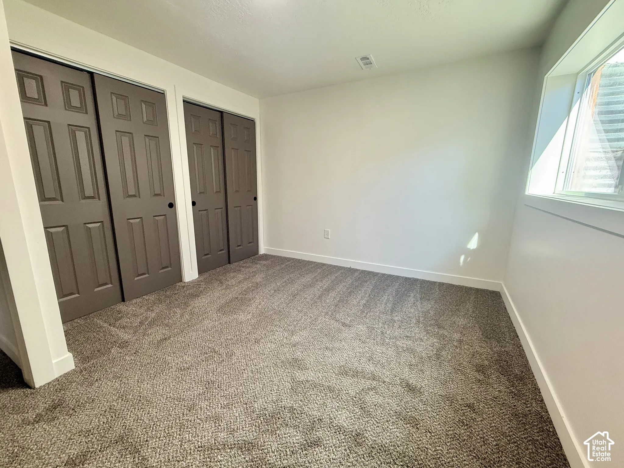 Neutral-toned wall-to-wall carpeting, dual sets of six-panel closet doors with matte black hardware, and an expansive window with white trim