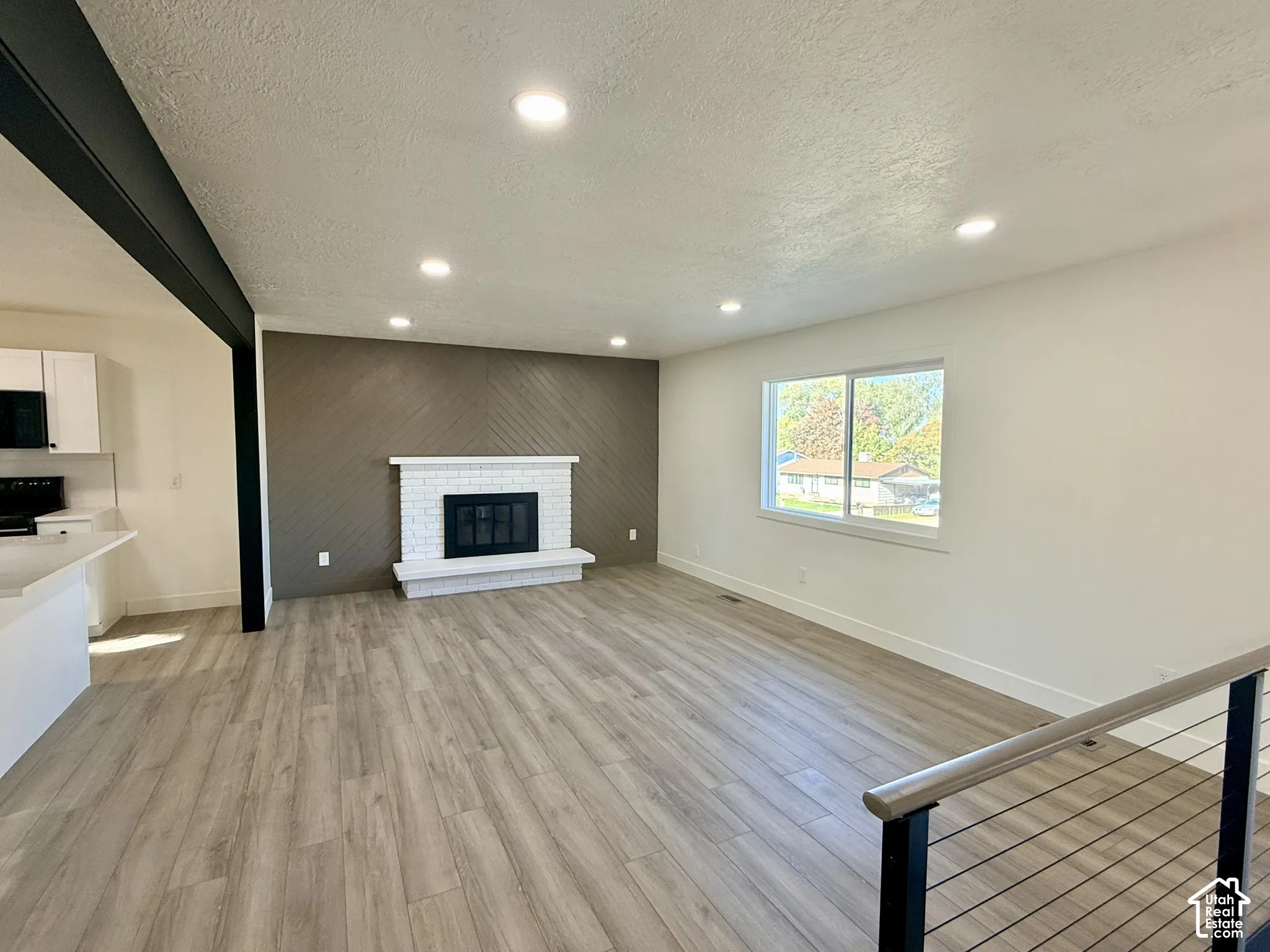 Living area featuring wood-finish flooring, a painted brick fireplace with a raised hearth, recessed lighting, and a prominent diagonal-patterned accent wall