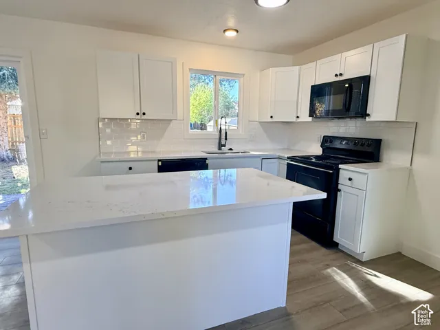 Kitchen featuring white cabinetry, solid-surface countertops, a subway tile backsplash, an island, and wood-finish flooring