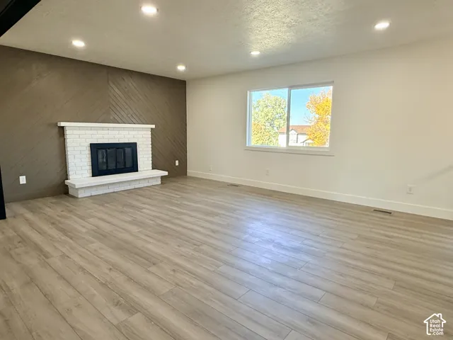 Wood-finish flooring throughout, white-painted brick fireplace with a raised hearth, diagonal wood-plank accent wall, recessed lighting, and large sliding window