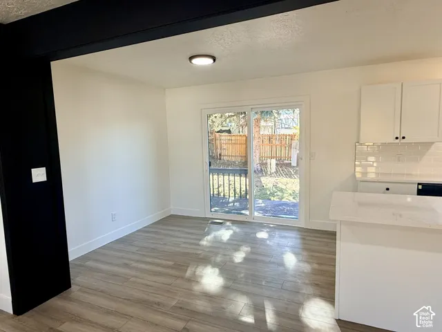 Wood-finish flooring, white cabinetry, tile backsplash, quartz-style countertops, and sliding glass patio doors