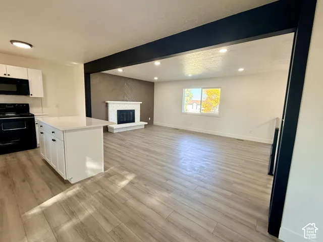 Kitchen featuring a central island with a solid-surface countertop, wood-finish flooring, recessed lighting, and a brick-surround fireplace with a hearth