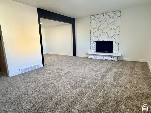 Floor-to-ceiling stone fireplace featuring a raised hearth, wall-to-wall carpeting, and a prominent dark-trimmed architectural opening