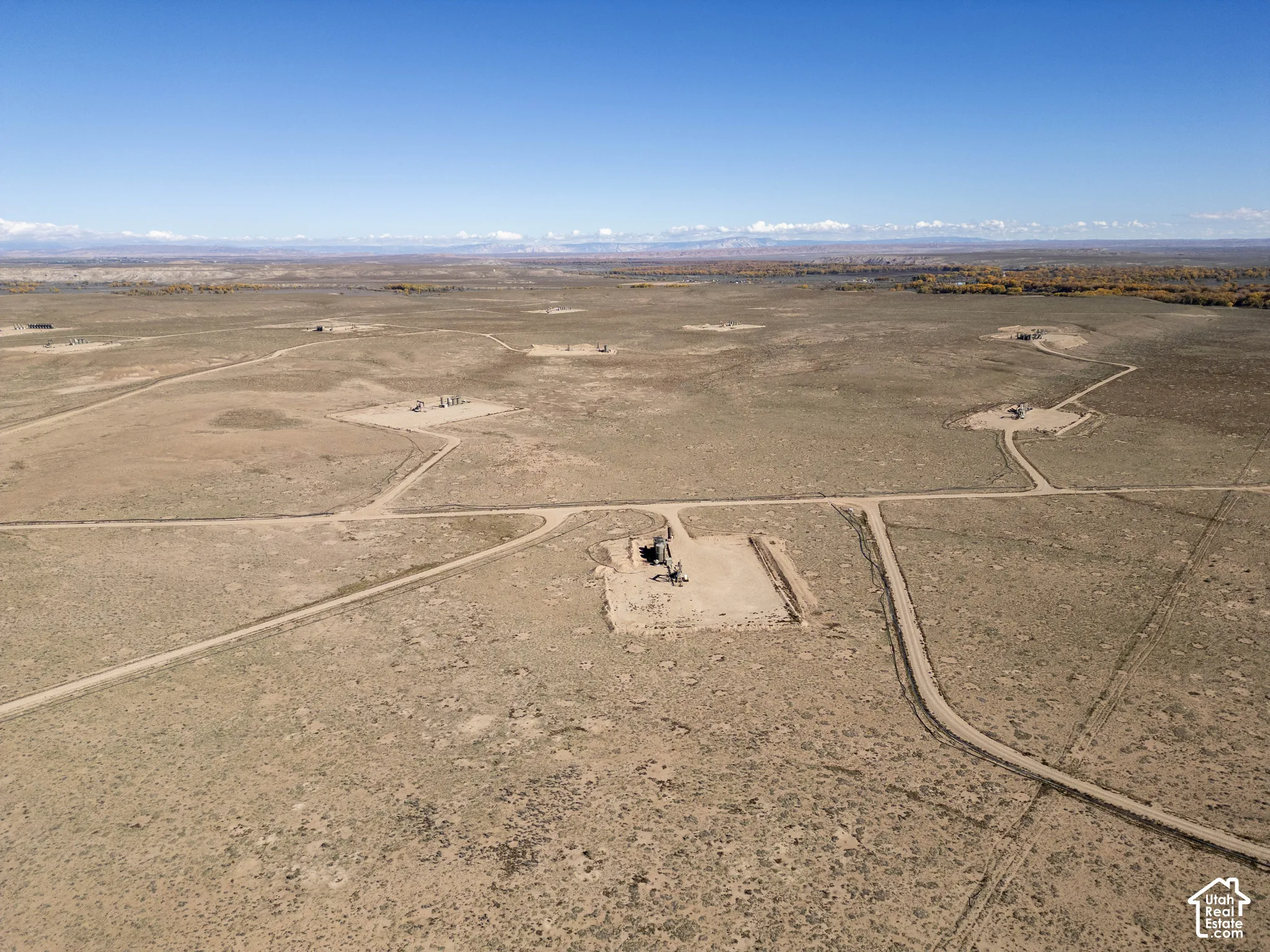Expansive desert acreage featuring established dirt road access, industrial infrastructure, and mountain range silhouettes on the horizon