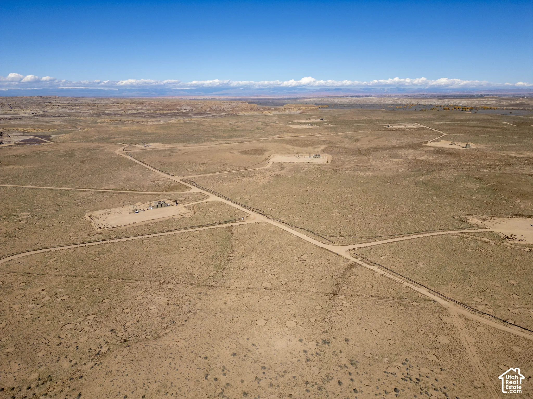 Expansive desert landscape featuring unpaved access roads and mountain horizon