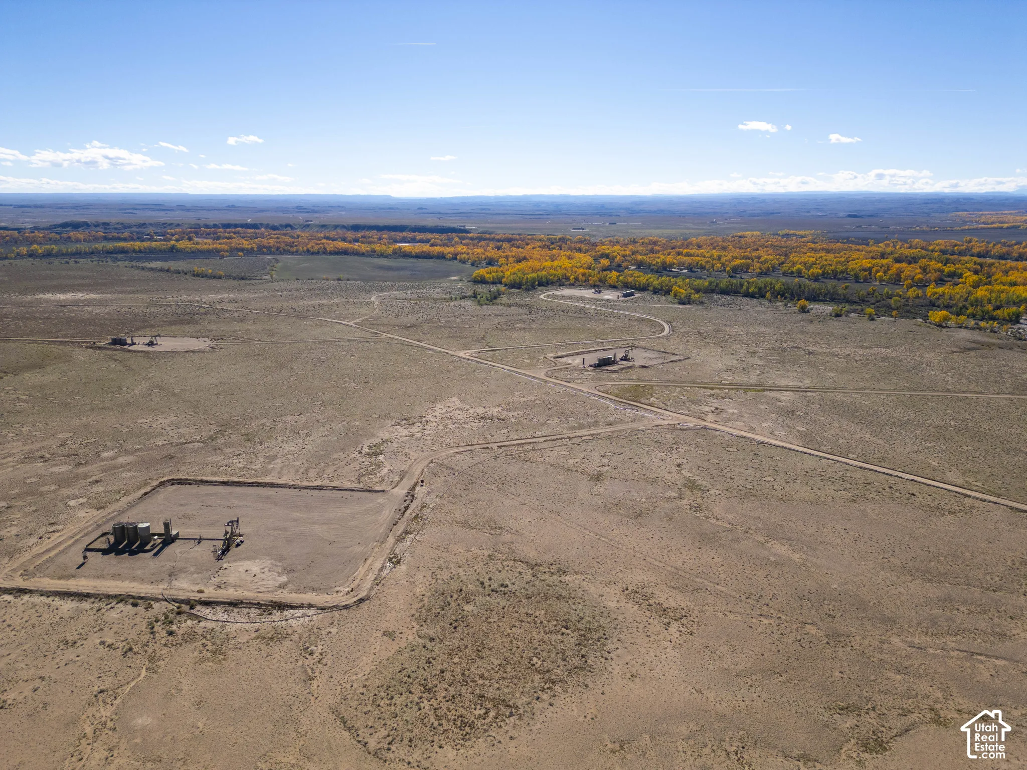 Expansive acreage featuring established dirt access roads, oil and gas infrastructure, and native high desert landscape with bordering deciduous trees
