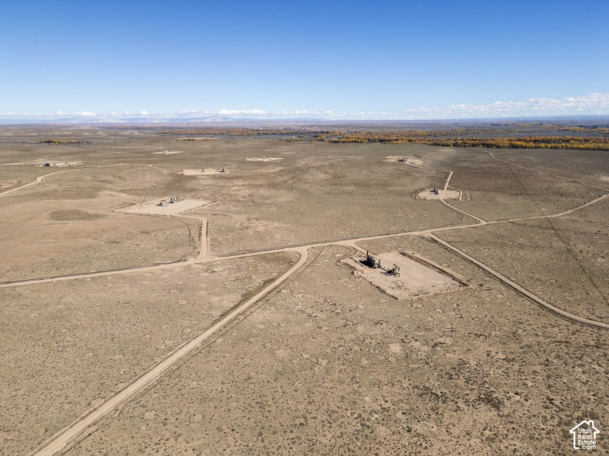 Expansive desert acreage featuring established dirt road access, multiple industrial well pads, and distant mountain backdrops