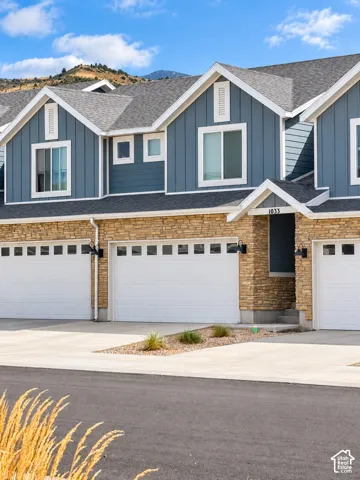 Multi-unit exterior featuring blue board-and-batten siding, horizontal stone veneer, gabled rooflines, attached multi-car garages, and mountain backdrop