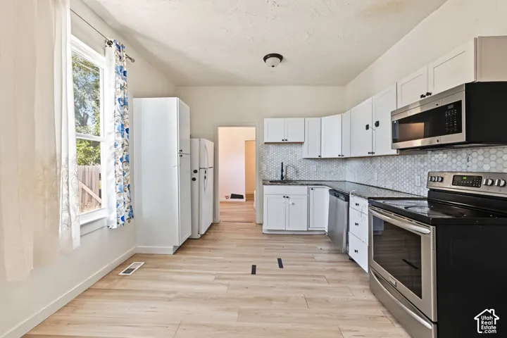 Kitchen featuring white shaker-style cabinetry, hexagon tile backsplash, wood-finish flooring, and stainless steel appliances