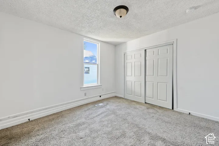 Neutral interior featuring textured ceilings, wall-to-wall carpeting, a single-hung window, and a built-in closet with six-panel sliding doors