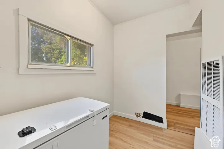 Interior space featuring wood-finish flooring, a horizontal sliding window with white trim, and a wall-mounted metal ventilation unit