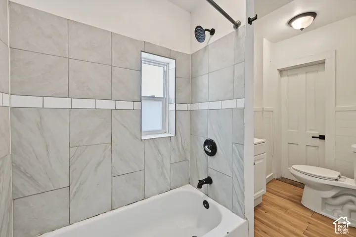 Bathtub featuring large-format grey tile surround with white subway tile accent, matte black plumbing fixtures, wood-finish flooring, and white paneled door